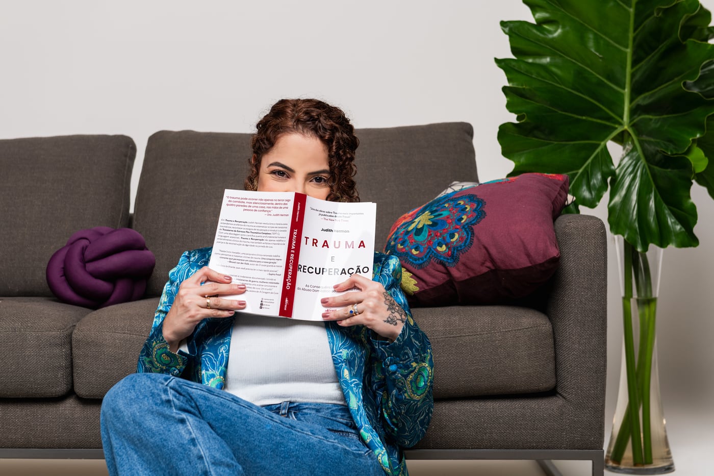 Danielle Nascimento sentada no sofá, com um livro nas mãos, em um ambiente acolhedor